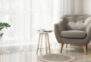 un fauteuil et un table d'appoint devant des rideaux voilage blanc