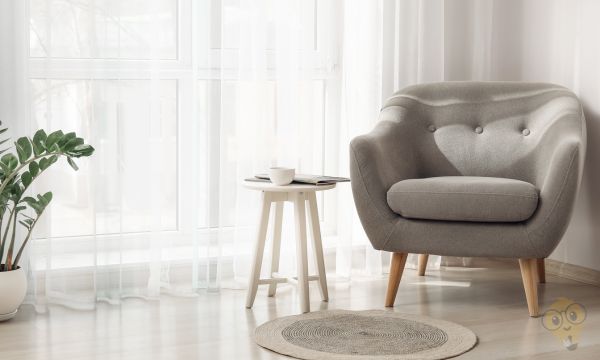 un fauteuil et un table d'appoint devant des rideaux voilage blanc